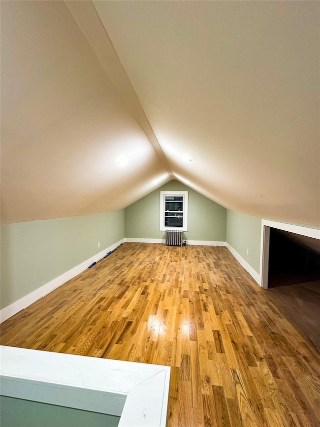 additional living space featuring hardwood / wood-style flooring, lofted ceiling, and radiator