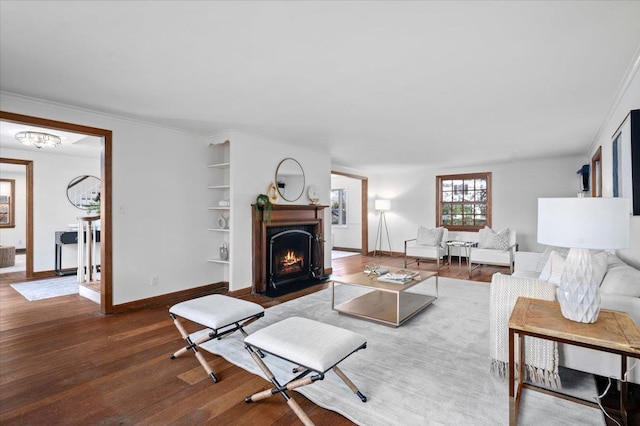 living room with baseboards, a fireplace with flush hearth, wood finished floors, crown molding, and built in shelves