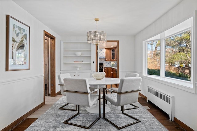 dining area featuring radiator, a notable chandelier, built in shelves, and wood finished floors