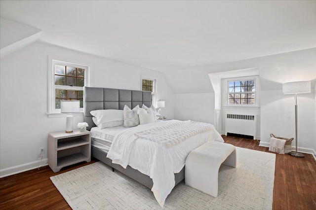 bedroom with vaulted ceiling, multiple windows, radiator heating unit, and wood finished floors