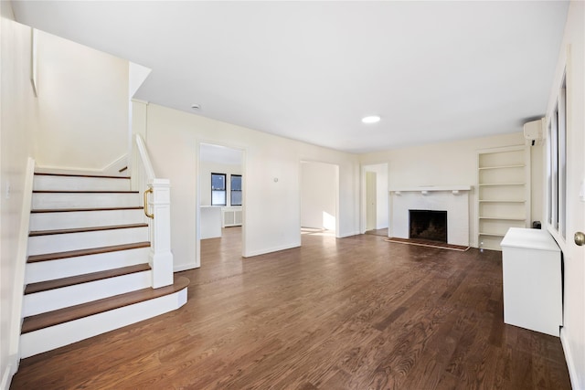 unfurnished living room featuring a wall mounted air conditioner, dark hardwood / wood-style flooring, and a brick fireplace