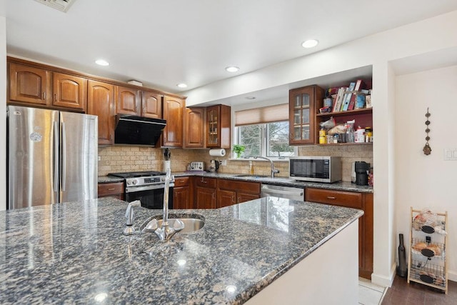 kitchen with backsplash, exhaust hood, sink, dark stone countertops, and stainless steel appliances