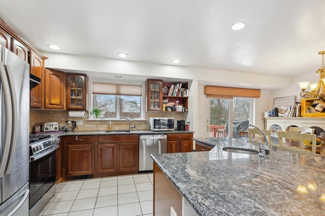 kitchen with sink, stainless steel appliances, tasteful backsplash, dark stone countertops, and light tile patterned floors