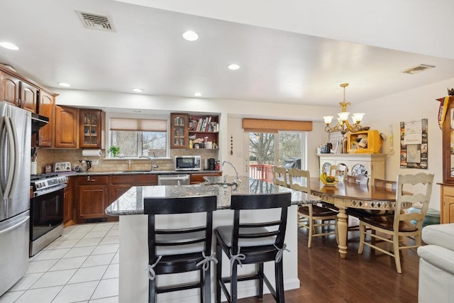 kitchen with hanging light fixtures, stainless steel appliances, a chandelier, a breakfast bar, and a center island with sink