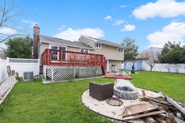 back of property with a yard, a fire pit, a storage unit, central air condition unit, and a wooden deck