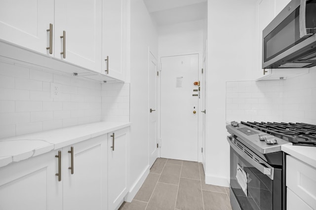 kitchen with light stone countertops, white cabinetry, light tile patterned floors, and stainless steel appliances