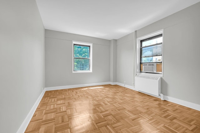 empty room with radiator heating unit, light parquet flooring, and cooling unit