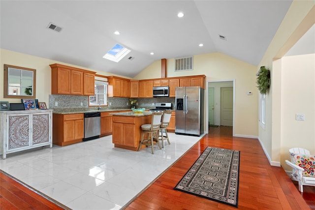 kitchen with stainless steel appliances, a breakfast bar, vaulted ceiling with skylight, decorative backsplash, and a kitchen island