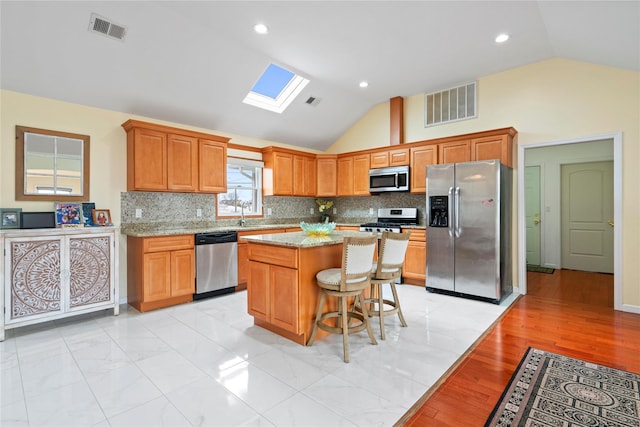 kitchen with a kitchen island, appliances with stainless steel finishes, vaulted ceiling with skylight, and a kitchen breakfast bar