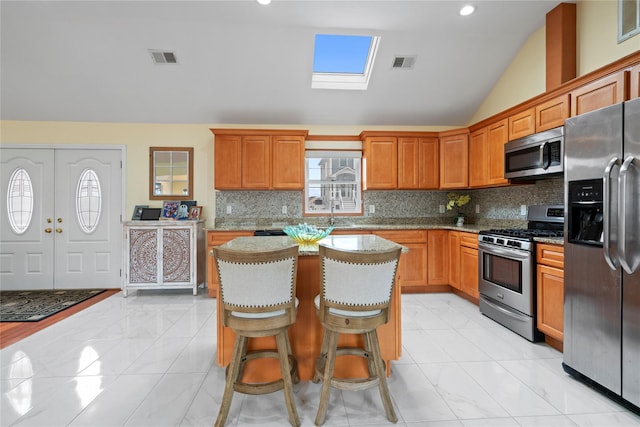 kitchen featuring stainless steel appliances, backsplash, a center island, and vaulted ceiling with skylight