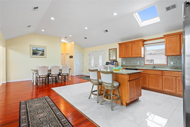 kitchen featuring sink, a center island, light stone counters, backsplash, and vaulted ceiling with skylight