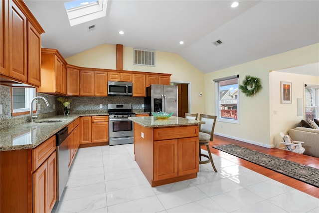 kitchen with sink, a kitchen island, vaulted ceiling with skylight, and appliances with stainless steel finishes