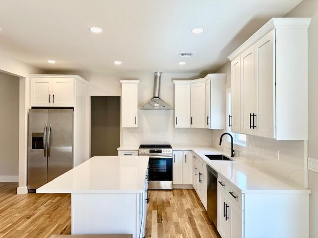 kitchen featuring a center island, white cabinets, wall chimney range hood, sink, and appliances with stainless steel finishes