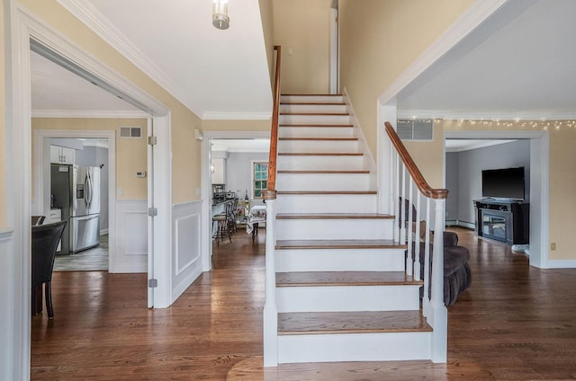 staircase featuring hardwood / wood-style floors, ornamental molding, and a fireplace