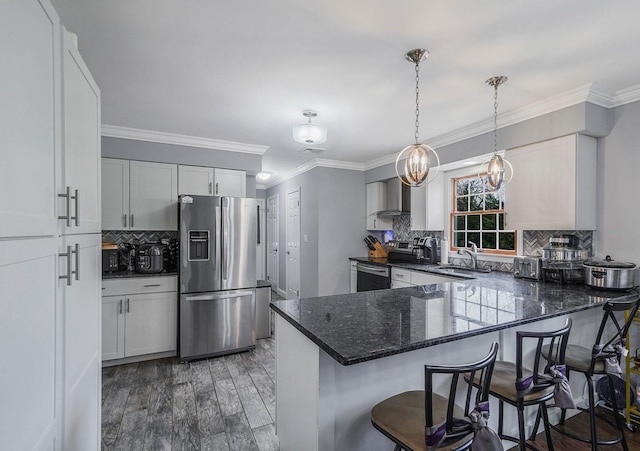 kitchen featuring wall chimney range hood, sink, appliances with stainless steel finishes, a kitchen bar, and kitchen peninsula