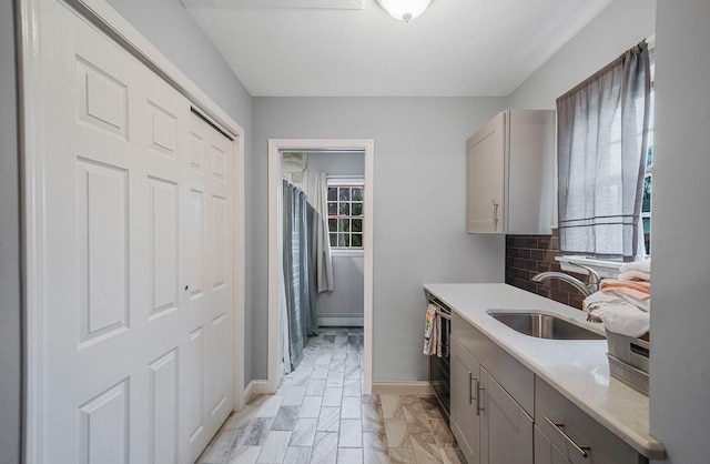 kitchen featuring gray cabinetry, dishwasher, sink, a baseboard heating unit, and backsplash