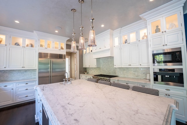 kitchen with white cabinetry, light stone counters, hanging light fixtures, and built in appliances