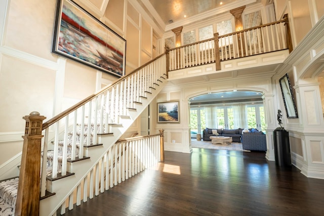 interior space with crown molding, a towering ceiling, wood-type flooring, and decorative columns