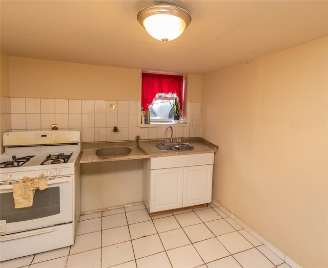 kitchen with light tile patterned flooring, white cabinetry, white gas range, and sink