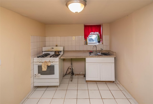 kitchen featuring white range with gas cooktop, white cabinets, backsplash, and sink