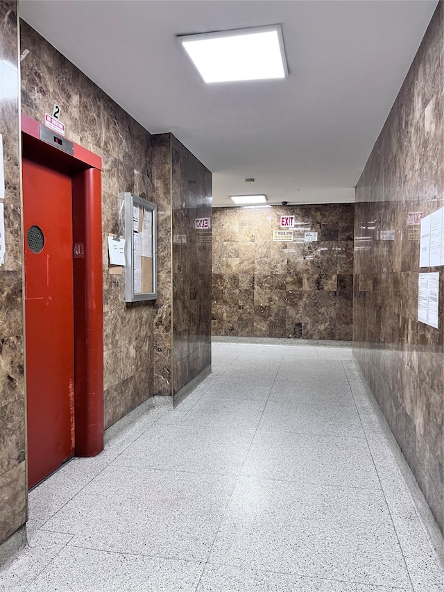 corridor featuring elevator and tile walls