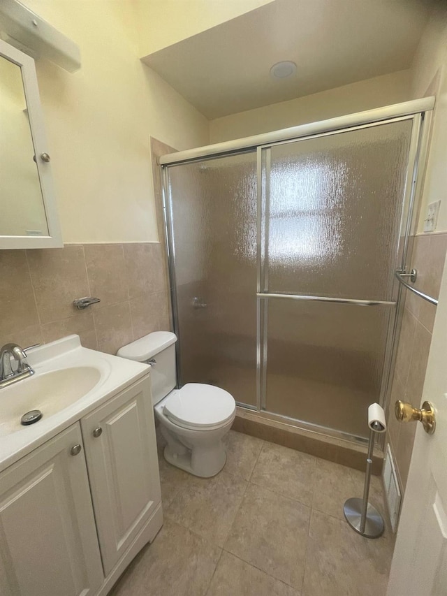 bathroom featuring vanity, a shower with door, tile patterned floors, toilet, and tile walls