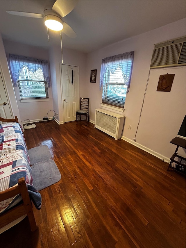 interior space featuring multiple windows, ceiling fan, radiator heating unit, and dark hardwood / wood-style flooring