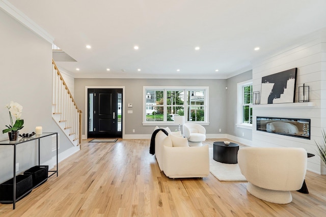 living room with a large fireplace, ornamental molding, and light wood-type flooring