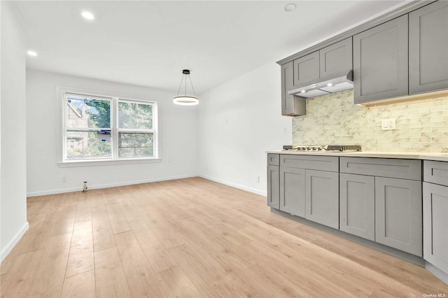 kitchen featuring stainless steel gas stovetop, hanging light fixtures, decorative backsplash, gray cabinets, and light wood-type flooring