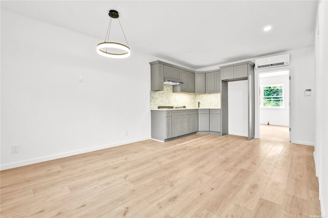 kitchen with decorative backsplash, light wood-type flooring, pendant lighting, an AC wall unit, and gray cabinets