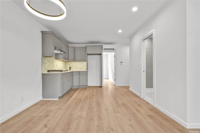 kitchen with gray cabinetry, light wood-type flooring, ventilation hood, and tasteful backsplash