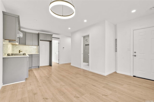 kitchen with gray cabinetry, decorative backsplash, light hardwood / wood-style floors, and a wall mounted AC