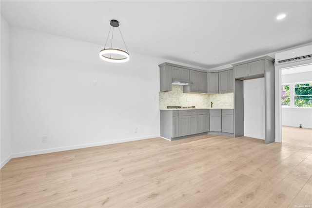 kitchen with gray cabinetry, gas stovetop, tasteful backsplash, light hardwood / wood-style floors, and a wall unit AC