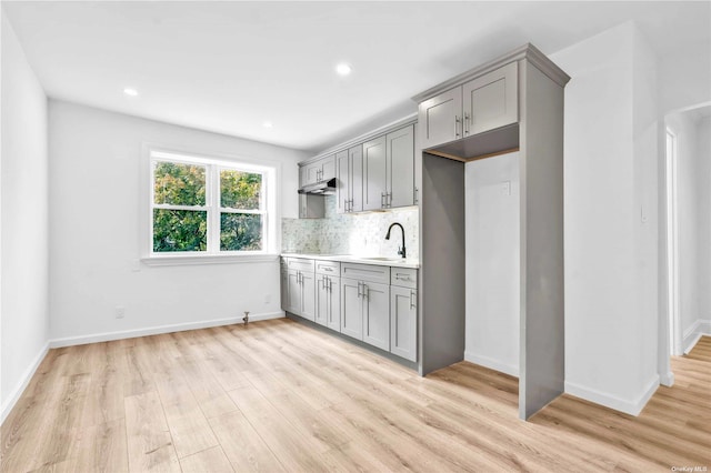 kitchen featuring decorative backsplash, light wood-type flooring, gray cabinetry, and sink