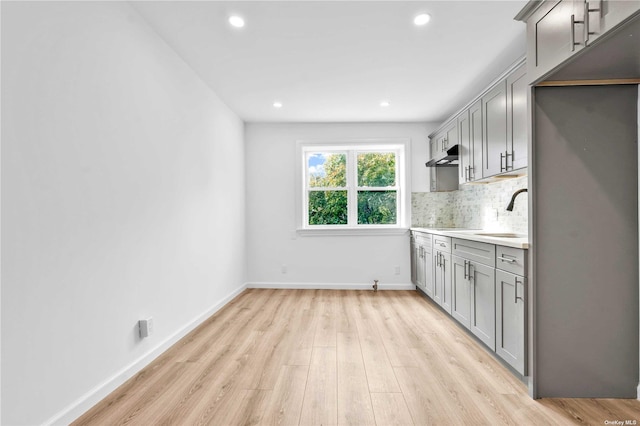 kitchen with light wood-type flooring, tasteful backsplash, gray cabinetry, and sink