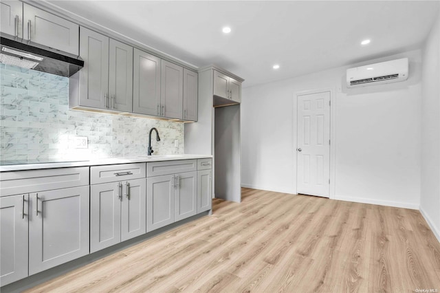 kitchen featuring an AC wall unit, sink, light hardwood / wood-style flooring, gray cabinets, and tasteful backsplash