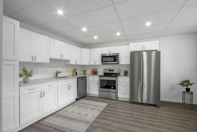 kitchen with appliances with stainless steel finishes, dark hardwood / wood-style floors, sink, white cabinets, and a drop ceiling