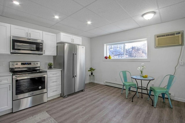 kitchen with a wall mounted air conditioner, light wood-type flooring, a baseboard radiator, stainless steel appliances, and white cabinets