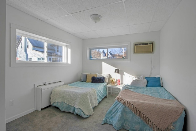 carpeted bedroom with a drop ceiling, radiator, and a wall mounted air conditioner