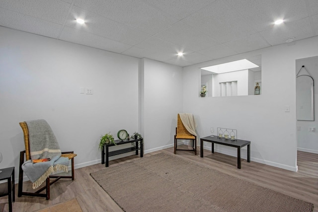 sitting room featuring a drop ceiling, light wood-type flooring, and a skylight