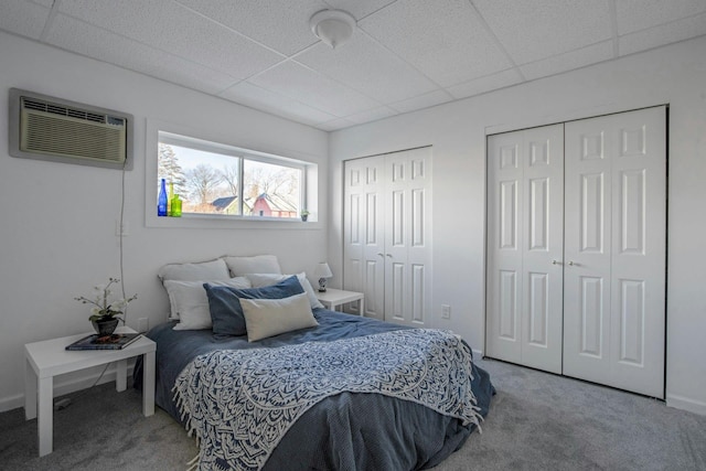 bedroom featuring a paneled ceiling, a wall unit AC, carpet, and two closets