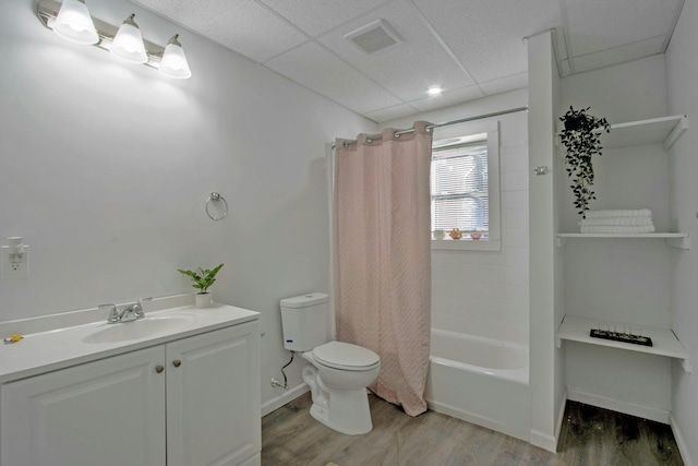 full bathroom with shower / tub combo, vanity, wood-type flooring, a drop ceiling, and toilet