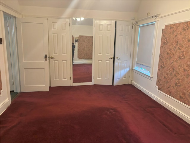 unfurnished bedroom with two closets, dark carpet, lofted ceiling, and baseboards