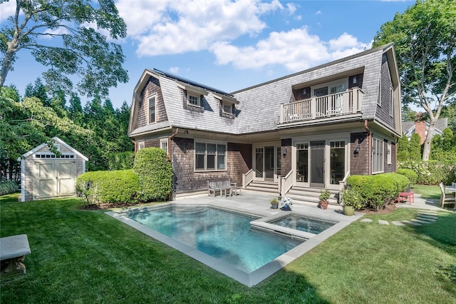 rear view of house featuring a swimming pool with hot tub, a balcony, a yard, a storage unit, and a patio area