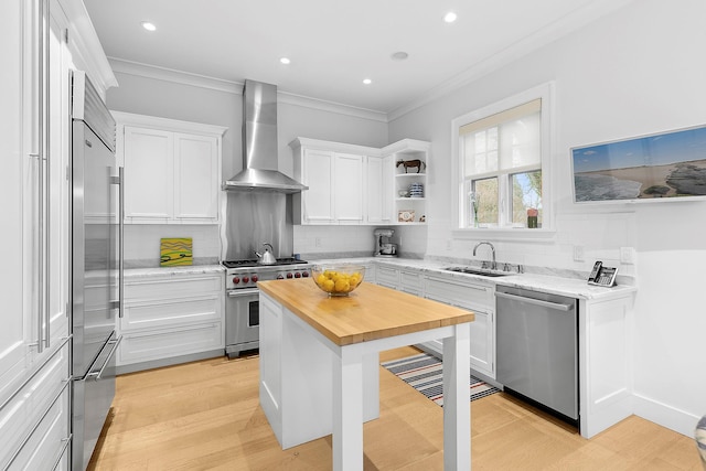 kitchen featuring sink, wall chimney range hood, high quality appliances, butcher block countertops, and white cabinetry