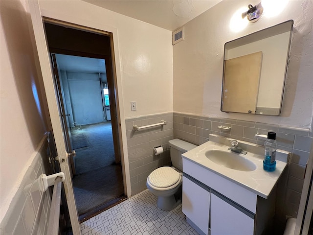 bathroom with toilet, tile patterned floors, vanity, and tile walls