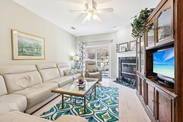 living room featuring a premium fireplace, light hardwood / wood-style floors, and ceiling fan