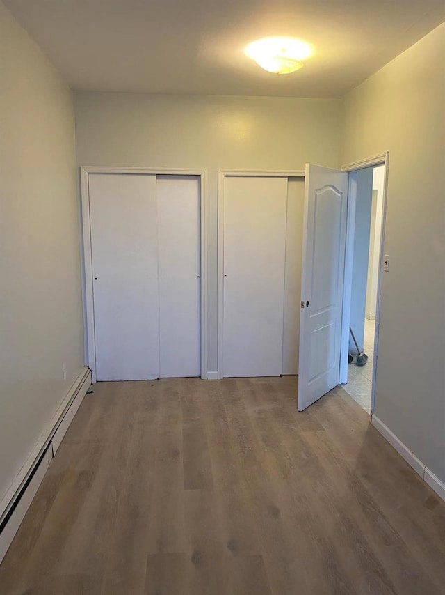 unfurnished bedroom featuring baseboard heating, wood-type flooring, and two closets