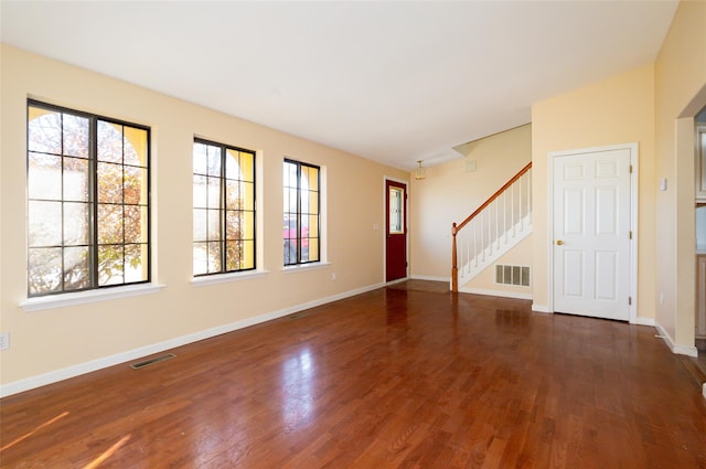 unfurnished living room with visible vents, baseboards, dark wood-type flooring, and stairs