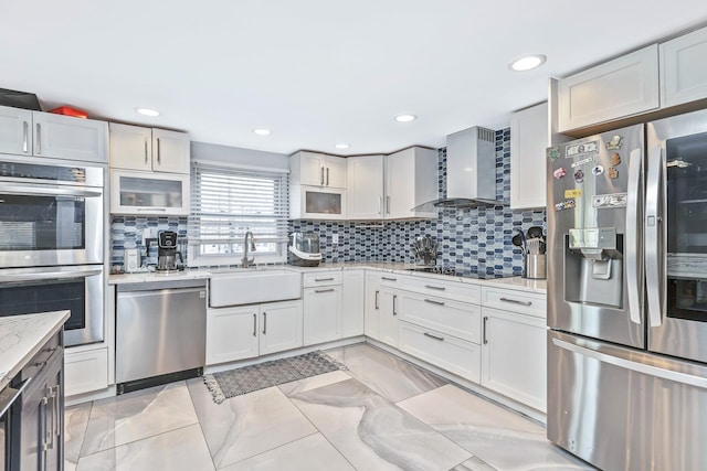 kitchen with backsplash, wall chimney range hood, sink, white cabinetry, and stainless steel appliances